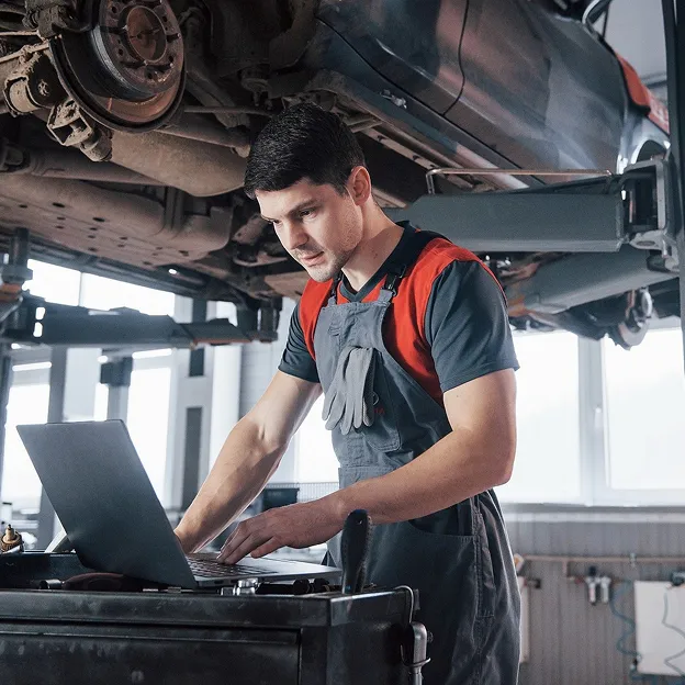 Mécanicien en salopette utilisant un ordinateur portable sous une voiture levée dans un garage à Azay-sur-Thouet dans les Deux-Sèvres 79