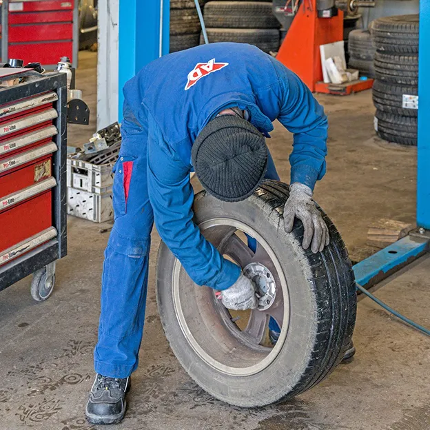 Mécanicien en combinaison bleue ajustant une roue de voiture dans un garage à Azay-sur-Thouet dans les Deux-Sèvres 79